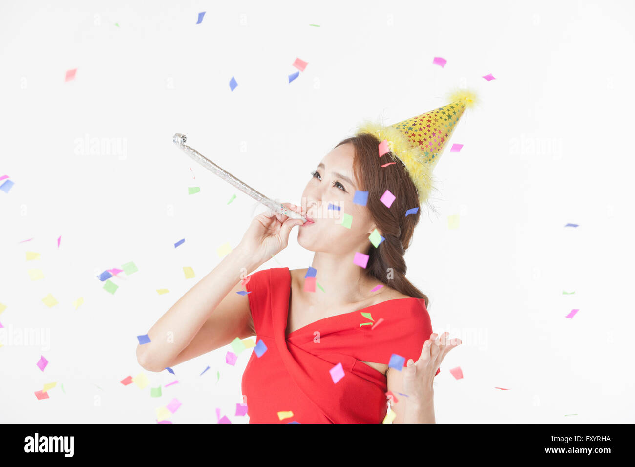 Portrait of young smiling woman blowing a party horn à la recherche jusqu'à confetti Banque D'Images