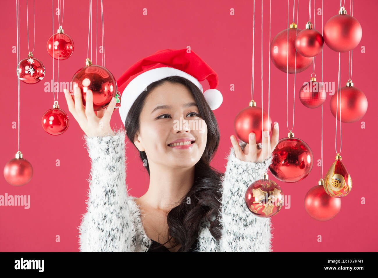 Portrait of young smiling woman wearing santa hat de toucher des boules de Noël jusqu'à la Banque D'Images