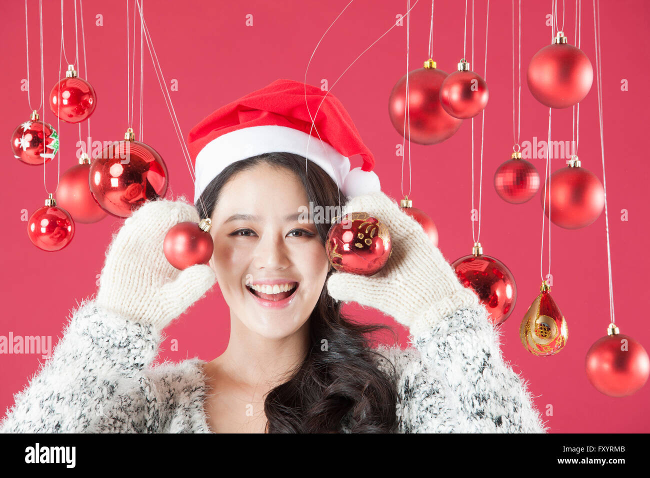 Portrait of young smiling woman wearing santa hat holding Christmas balls fixant à l'avant Banque D'Images