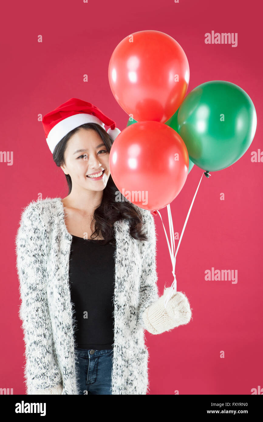Portrait of young smiling woman wearing santa hat et mitaines holding balloons fixant à l'avant Banque D'Images