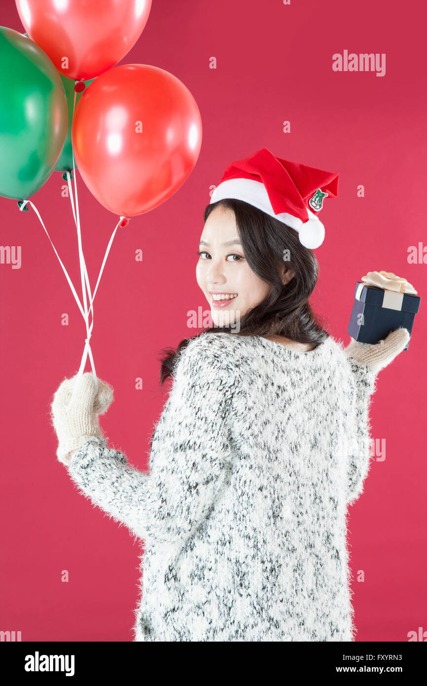 Retour de young smiling woman wearing santa hat et mitaines holding balloons et présenter fort à l'arrière Banque D'Images