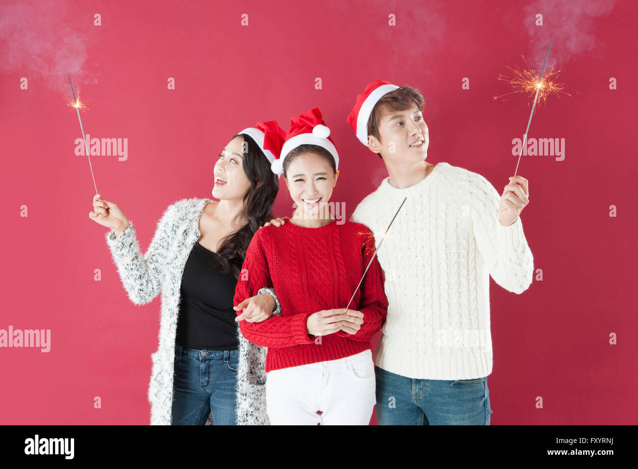 Portrait de trois jeunes smiling people wearing santa hats holding jusqu'à Fireworks Banque D'Images