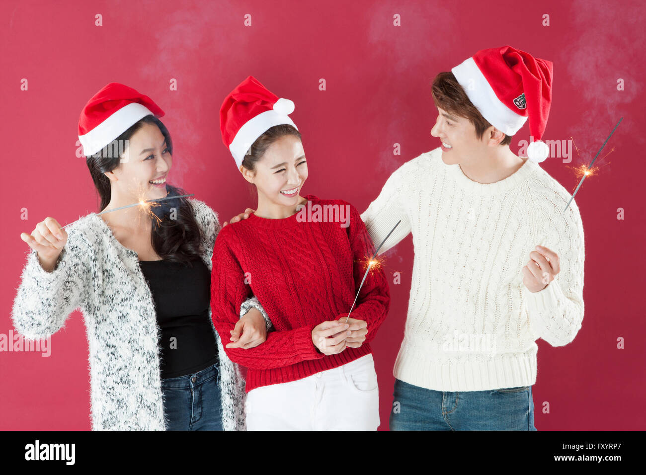 Portrait de trois jeunes smiling people wearing santa hats holding d'artifice face à face Banque D'Images
