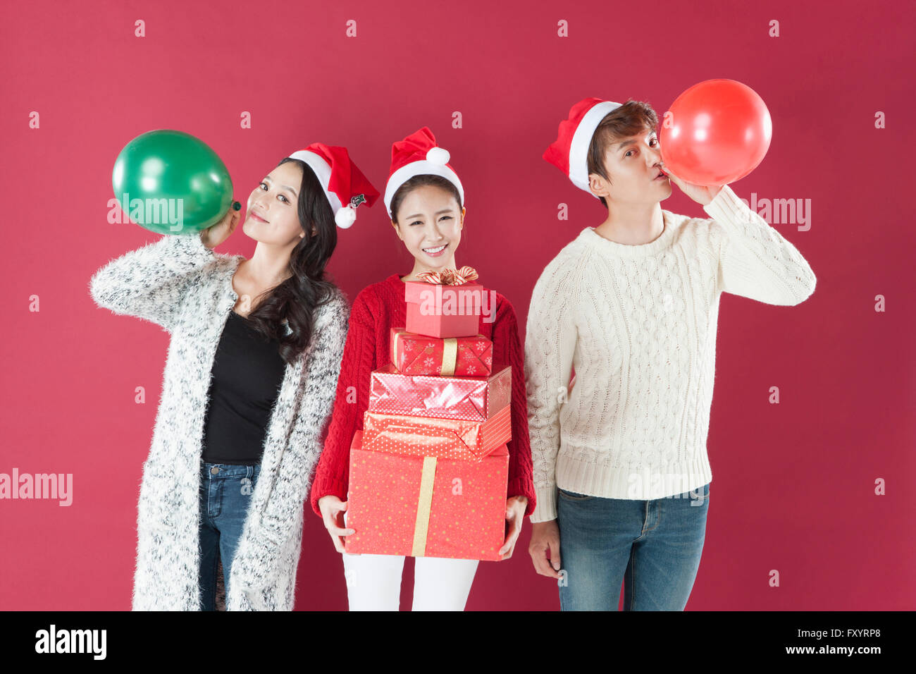 Trois jeunes smiling people wearing santa hats avec des ballons et des boîtes empilées présent Banque D'Images