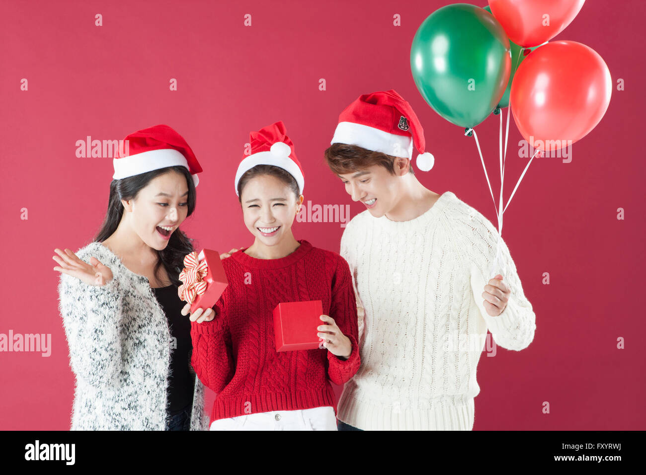 Portrait de trois jeunes smiling people wearing santa hats holding present fort et des ballons Banque D'Images