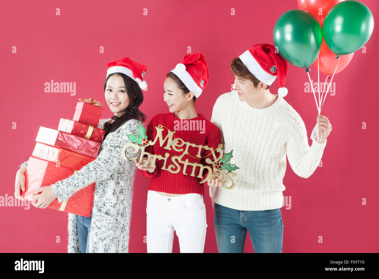 Trois jeunes gens souriants avec les boîtes empilées présents, les ballons et le message de Joyeux Noël Banque D'Images