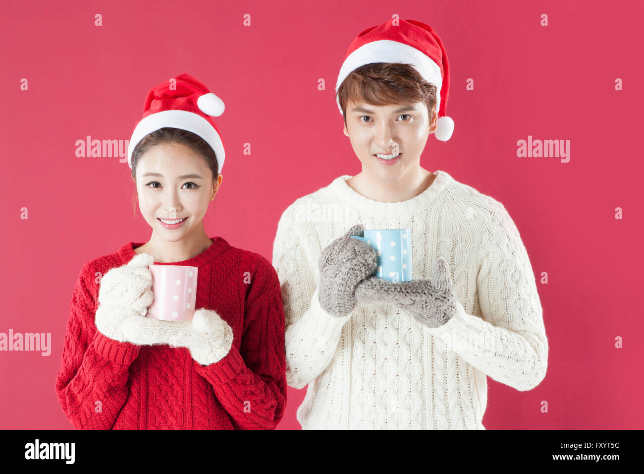 Portrait of young woman wearing santa hats et mitaines holding mugs regarder/ Banque D'Images