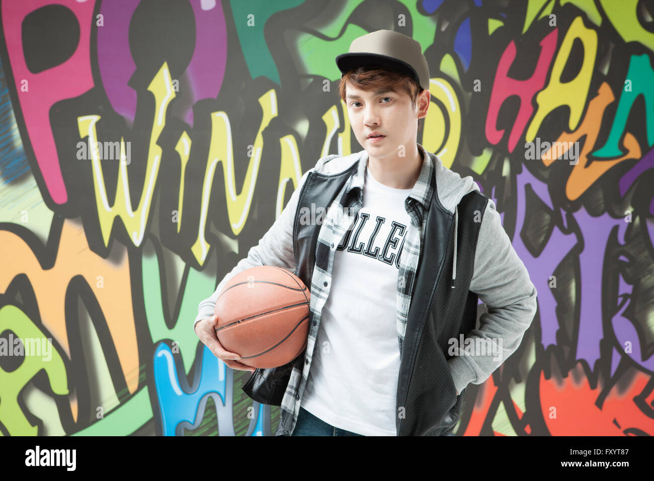 Portrait de jeune homme dans un style hip-hop avec un basket-ball contre l'art du graffiti Banque D'Images