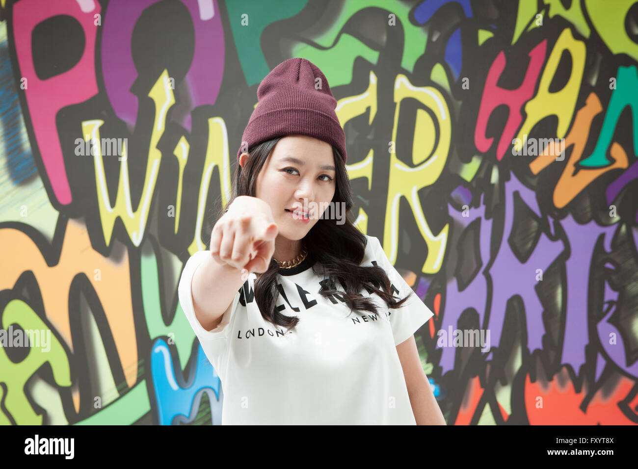 Portrait de jeune femme au style hip-hop pointant vers l'avant contre l'art du graffiti Banque D'Images