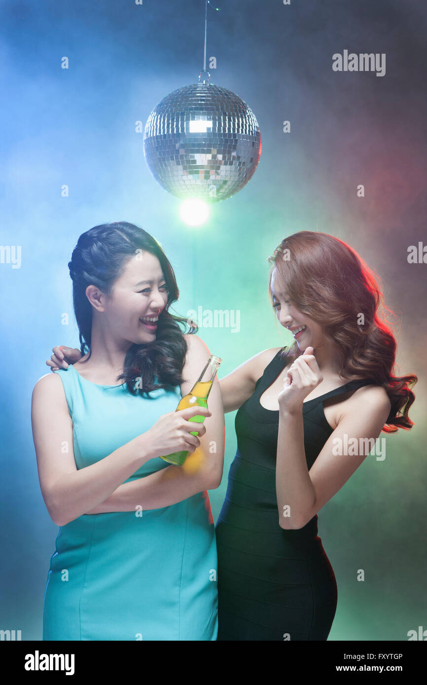 Deux jeunes femmes sourire danse avec bouteille de bière sous une boule miroir Banque D'Images