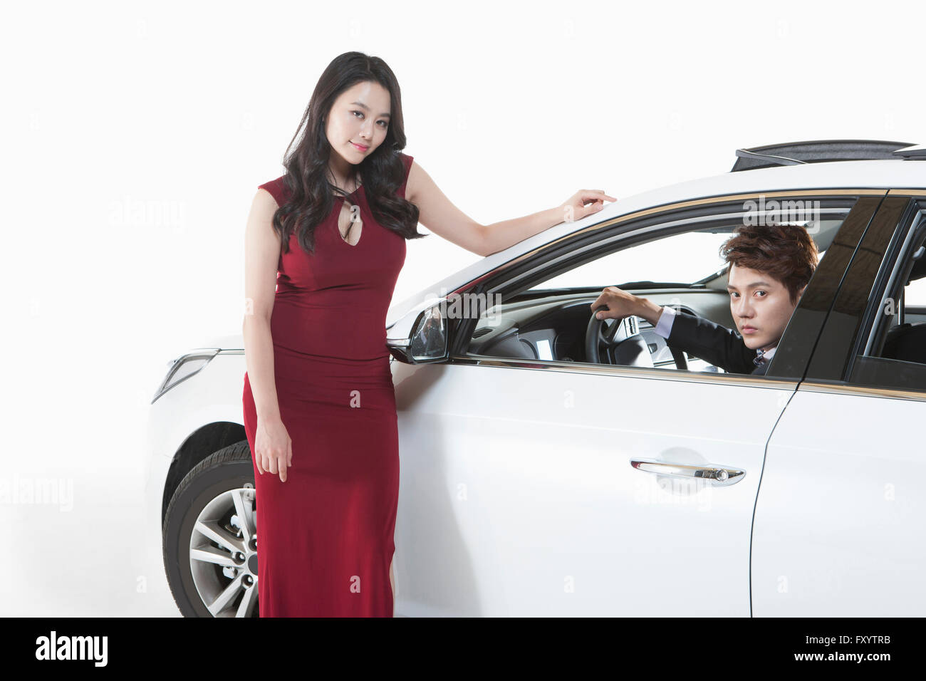 Jeune femme en robe rouge devant de voiture et jeune homme en costume dans la voiture fixant à l'avant Banque D'Images
