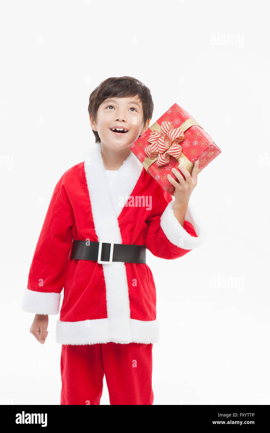 Smiling boy in Santa's clothes hoding un présent fort looking up Banque D'Images