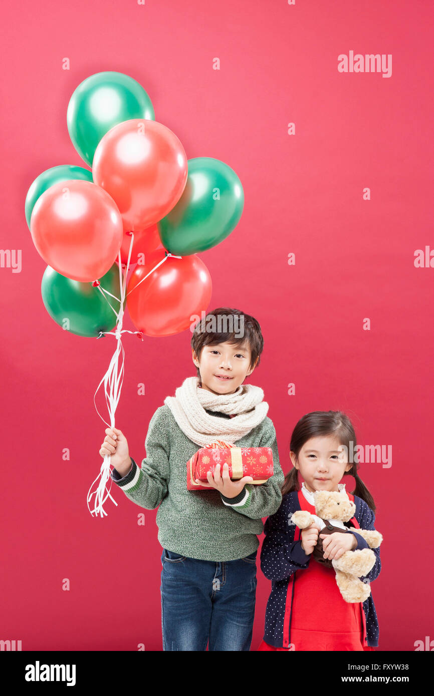 Korean boy and girl holding balloons, présent fort et un ours regardant à l'avant avec le sourire Banque D'Images