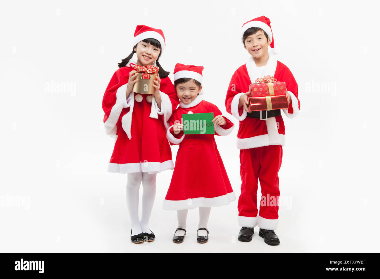 Trois enfants souriants dans Santa's clothes debout avec les boîtes et les présenter à l'avant de la carte Banque D'Images