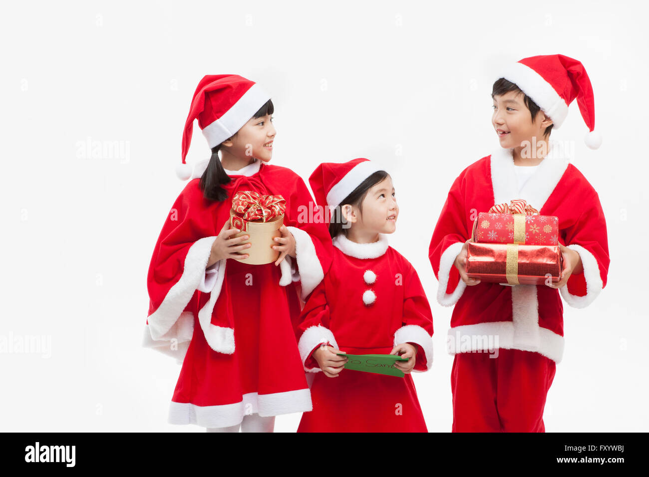 Trois enfants souriants dans Santa's clothes holding présente des boîtes et carte face à face Banque D'Images