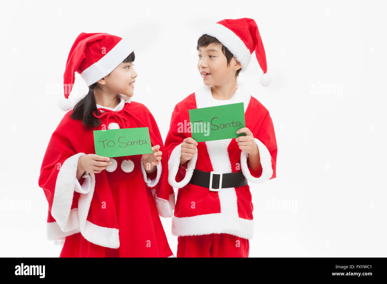 Vue latérale du smiling boy and girl in Santa's clothes holding cartes pour Santa face à face Banque D'Images