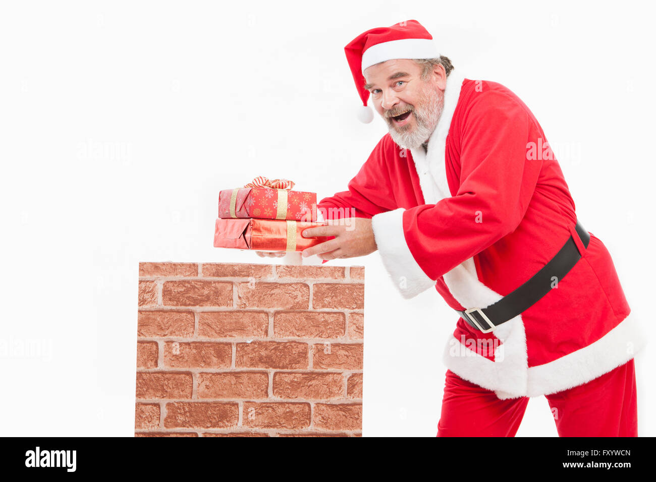 Vue latérale du smiling Santa mettant un présent fort dans une cheminée à regarder/ Banque D'Images