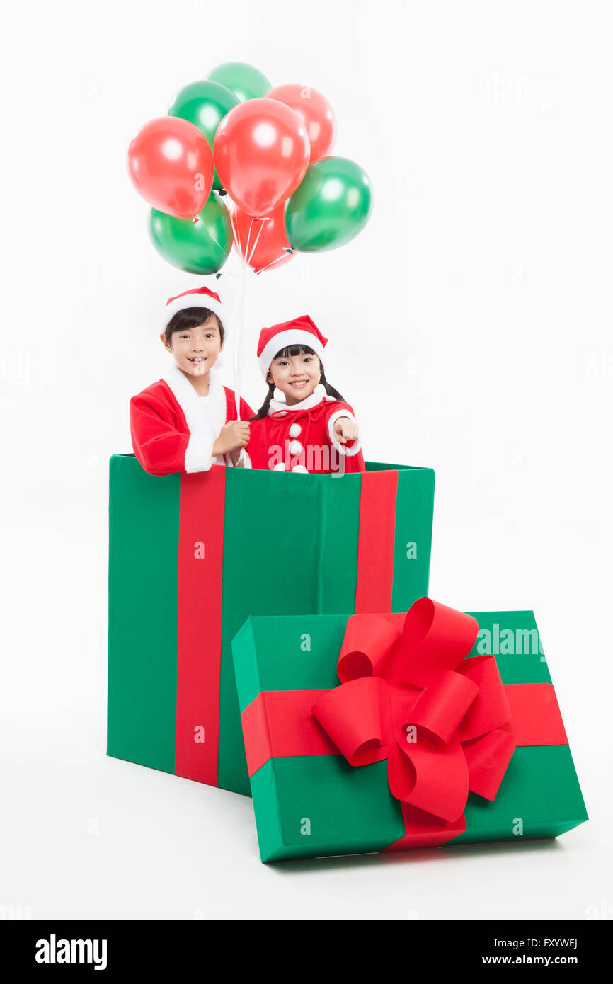 Portrait of smiling boy and girl in Santa's clothes holding balloons dans un grand présent fort regarder/ Banque D'Images
