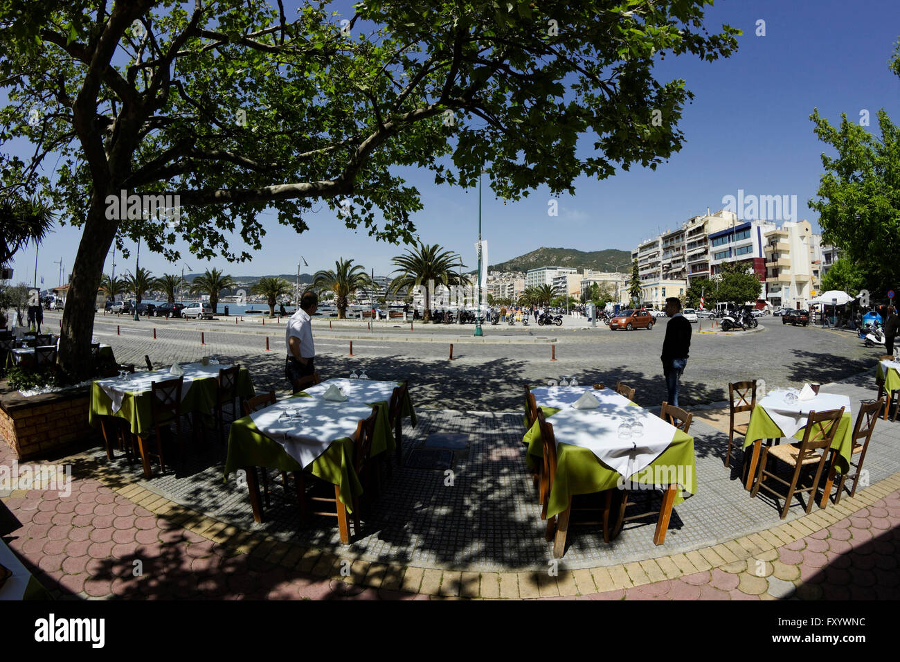 Restaurant grec rangées de tables vides alignés, sur le trottoir ombragé de Panagia, district de la ville de Kavala, Grèce waterfront port Banque D'Images