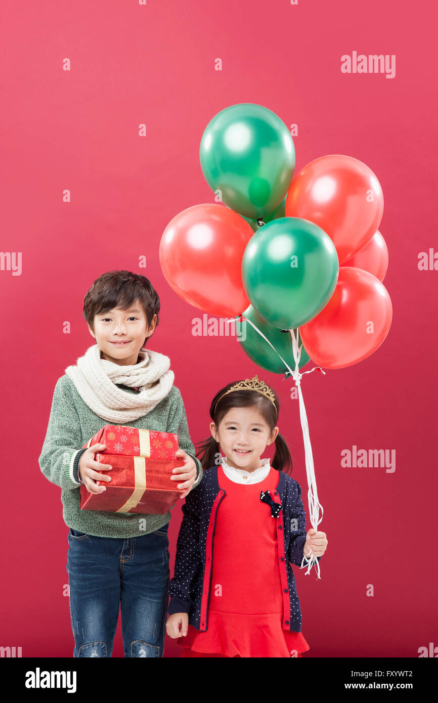 Smiling boy avec boîtes empilées présents et smiling girl holding balloons debout à regarder/ Banque D'Images