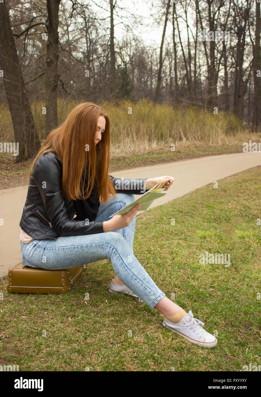 Ginger femme assise sur vieille valise, l'exploration de route en plein air dans le parc en Europe Banque D'Images