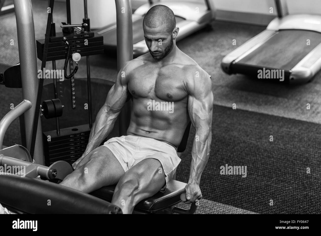 Jeune homme attrayant faisant les jambes avec la machine In Gym Banque D'Images