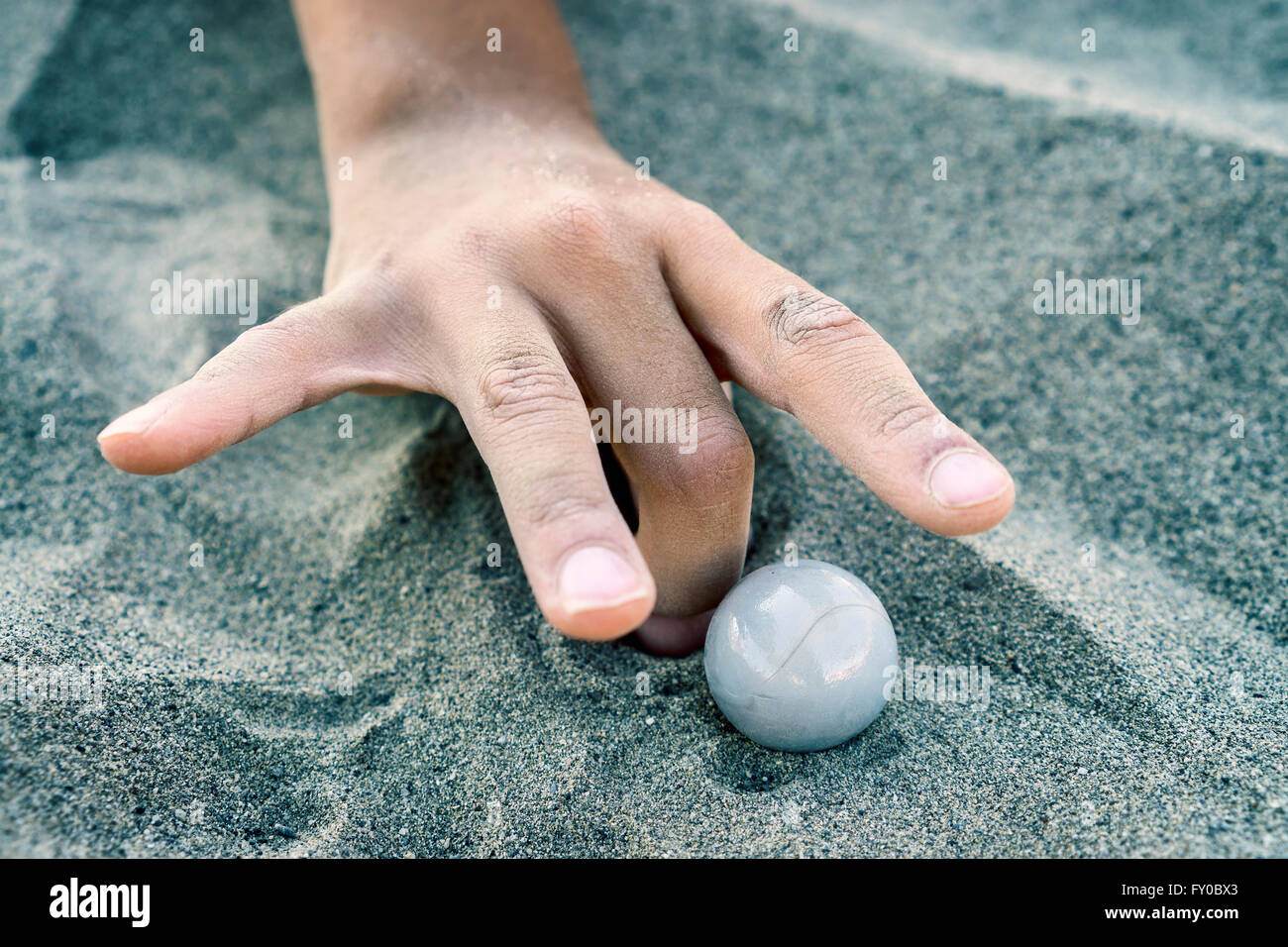 Main d'un enfant jouer avec des billes dans le sable Banque D'Images