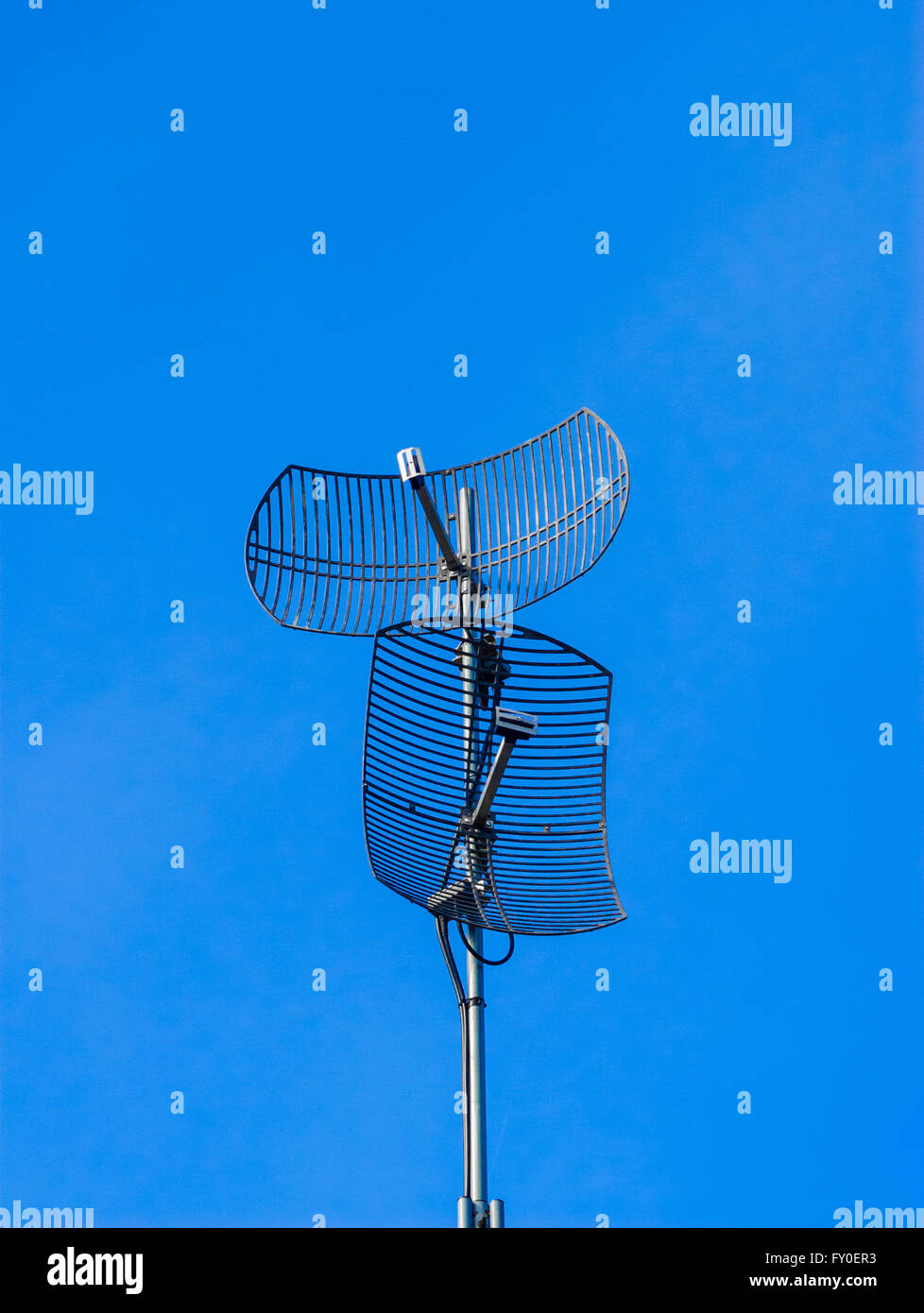 Deux antennes paraboliques pointant dans des directions différentes sur ciel bleu. Banque D'Images