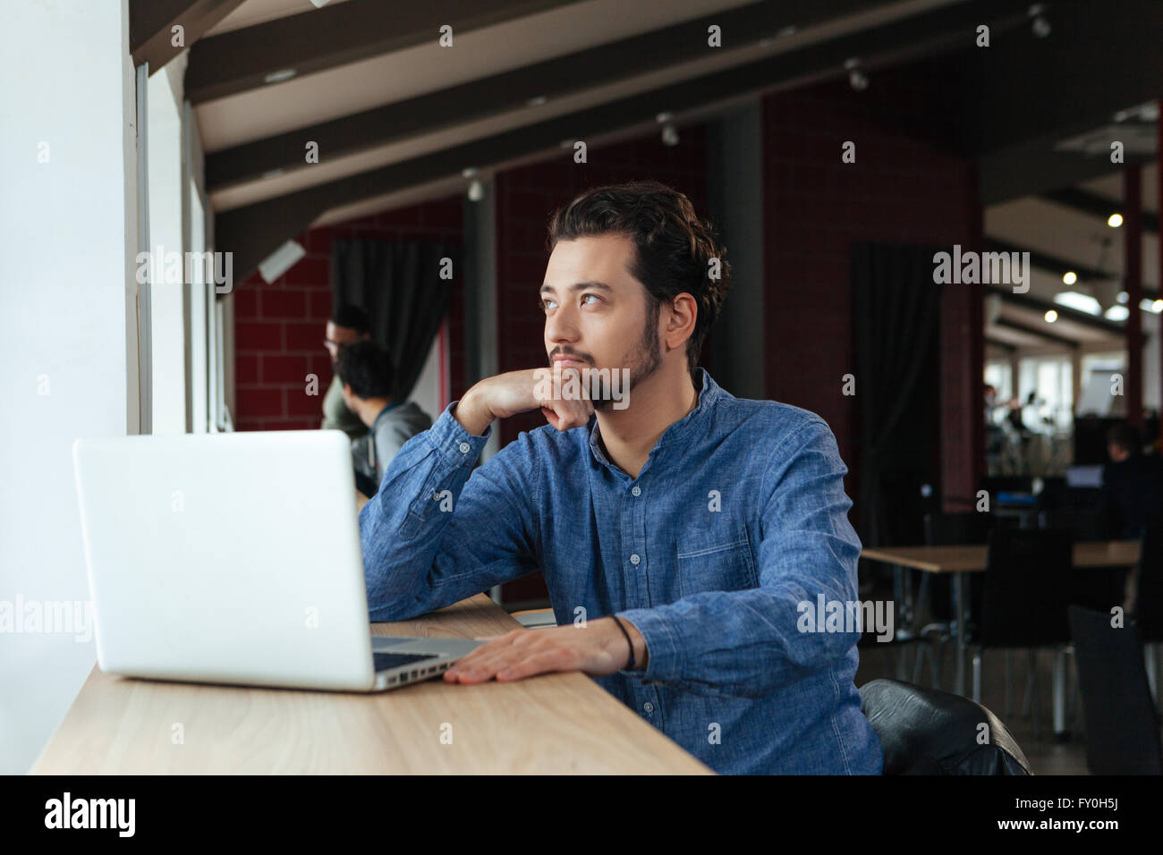 Pensive l'homme assis à la table with laptop computer in office Banque D'Images