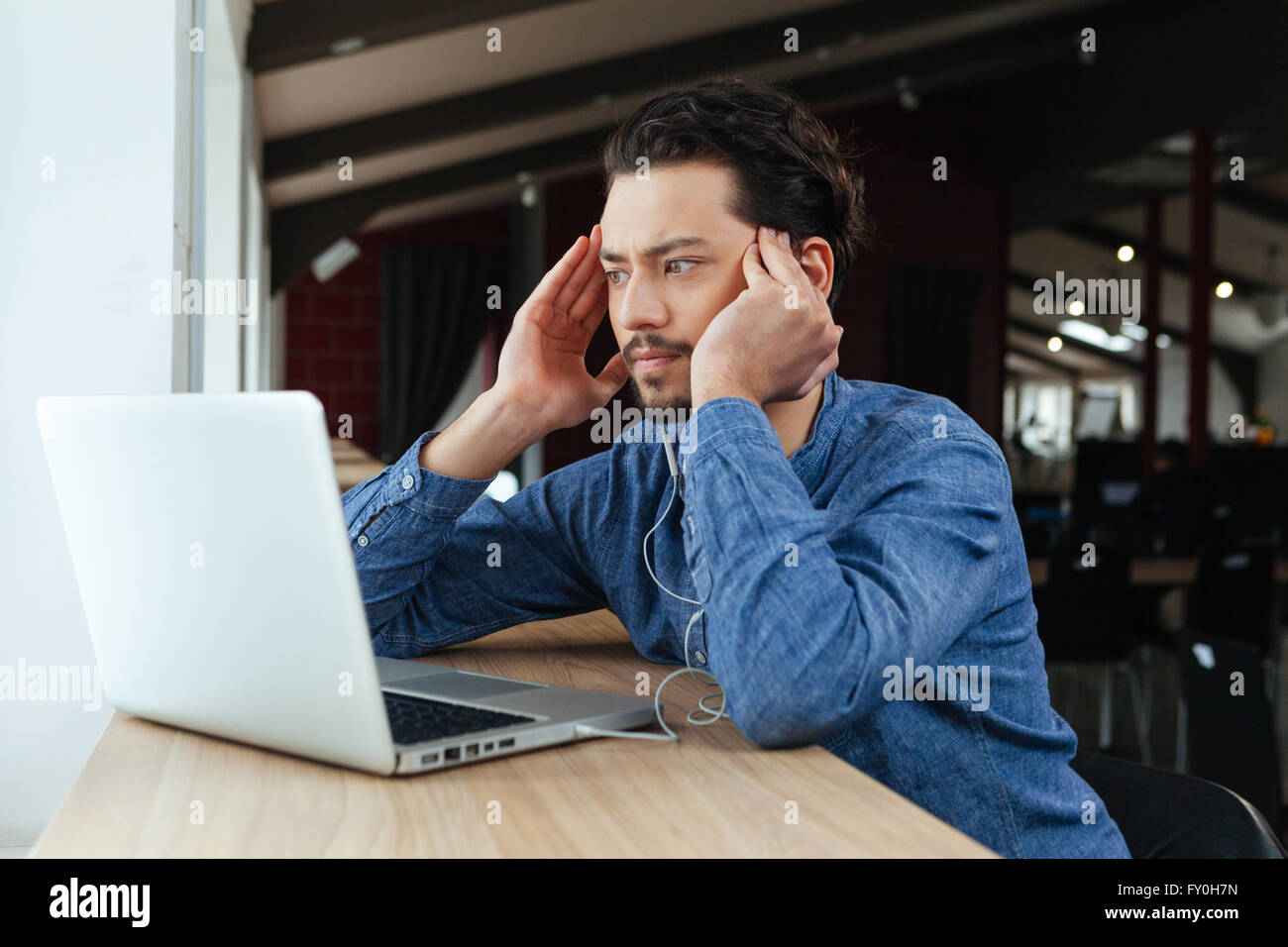 Un homme assis le tableau avec ordinateur portable et bureau en pensant à quelque chose de Banque D'Images