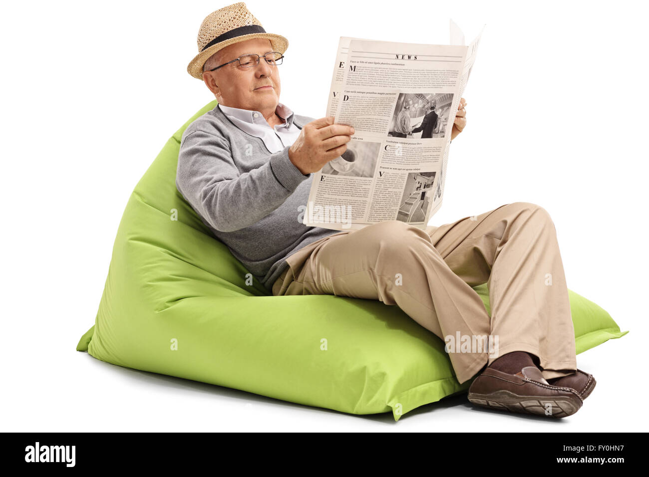 Relaxed mature man lire un journal assis sur un pouf vert isolé sur fond blanc Banque D'Images