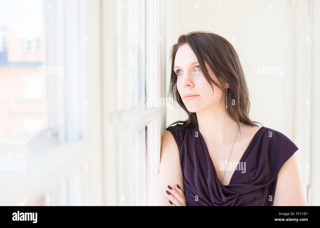 Femme en robe noire debout par une fenêtre, regardant ailleurs. Concept de la solitude, une réflexion sérieuse et de tristesse. Banque D'Images