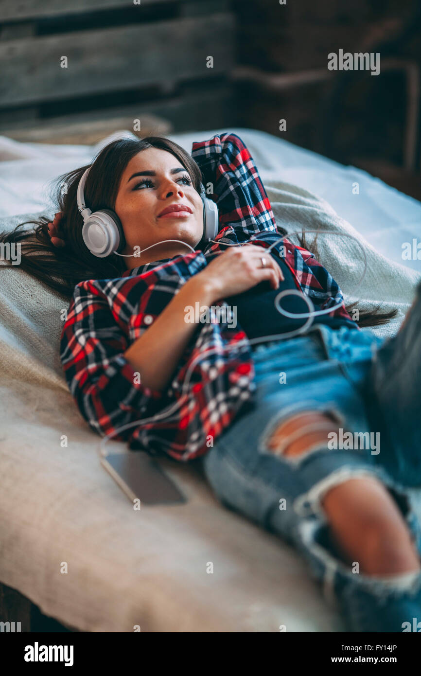 Trendy young woman listening music while lying on bed at home Banque D'Images
