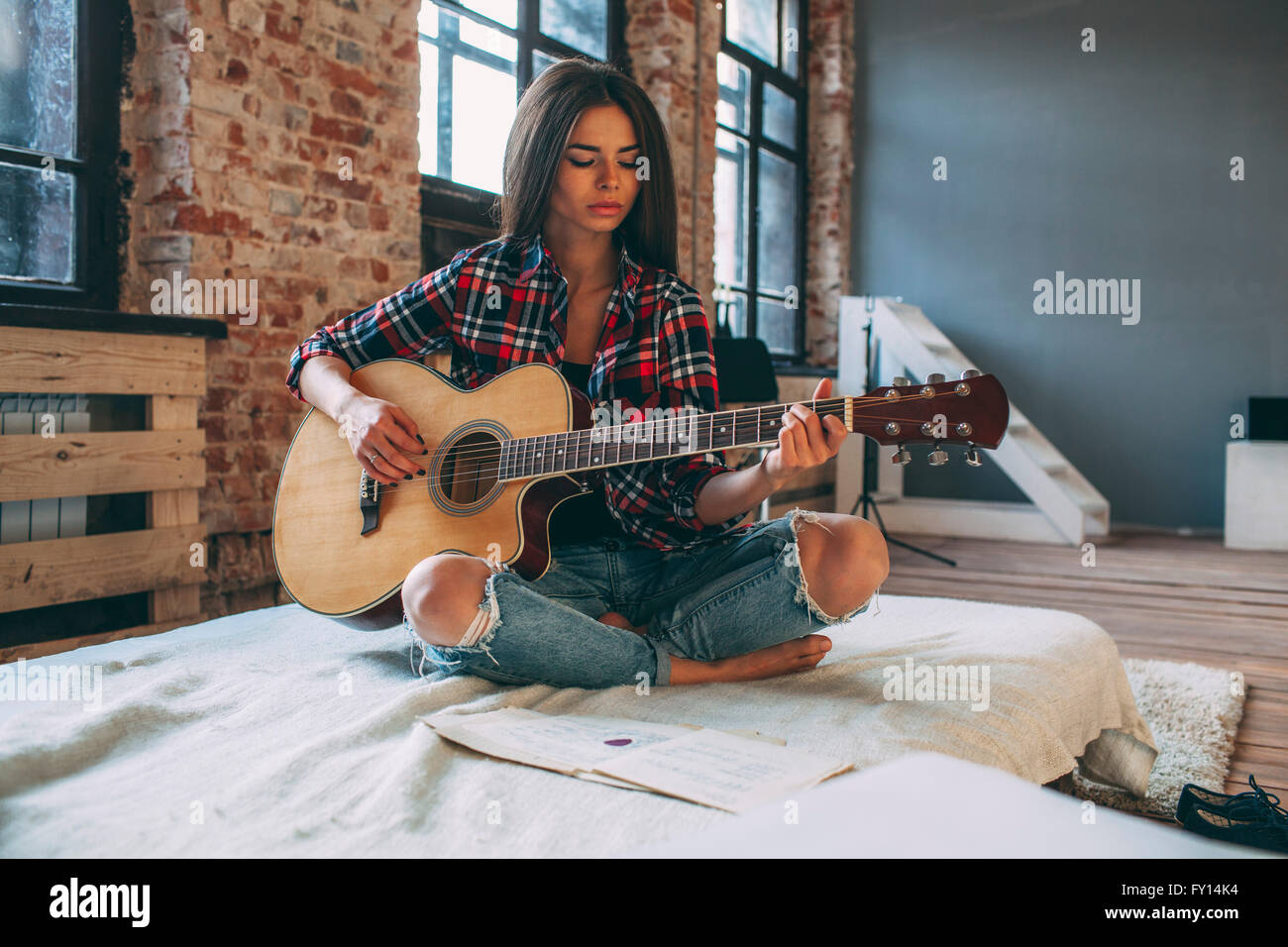 Young woman playing guitar while sitting on bed at home Banque D'Images