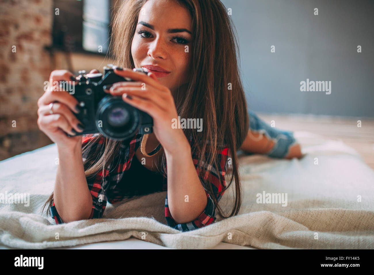 Portrait of young woman holding camera Nikon en position couchée sur le lit chez lui Banque D'Images