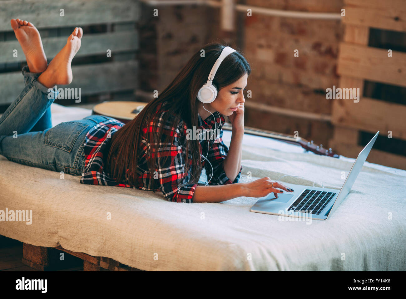 Young woman listening music while using laptop on bed at home Banque D'Images