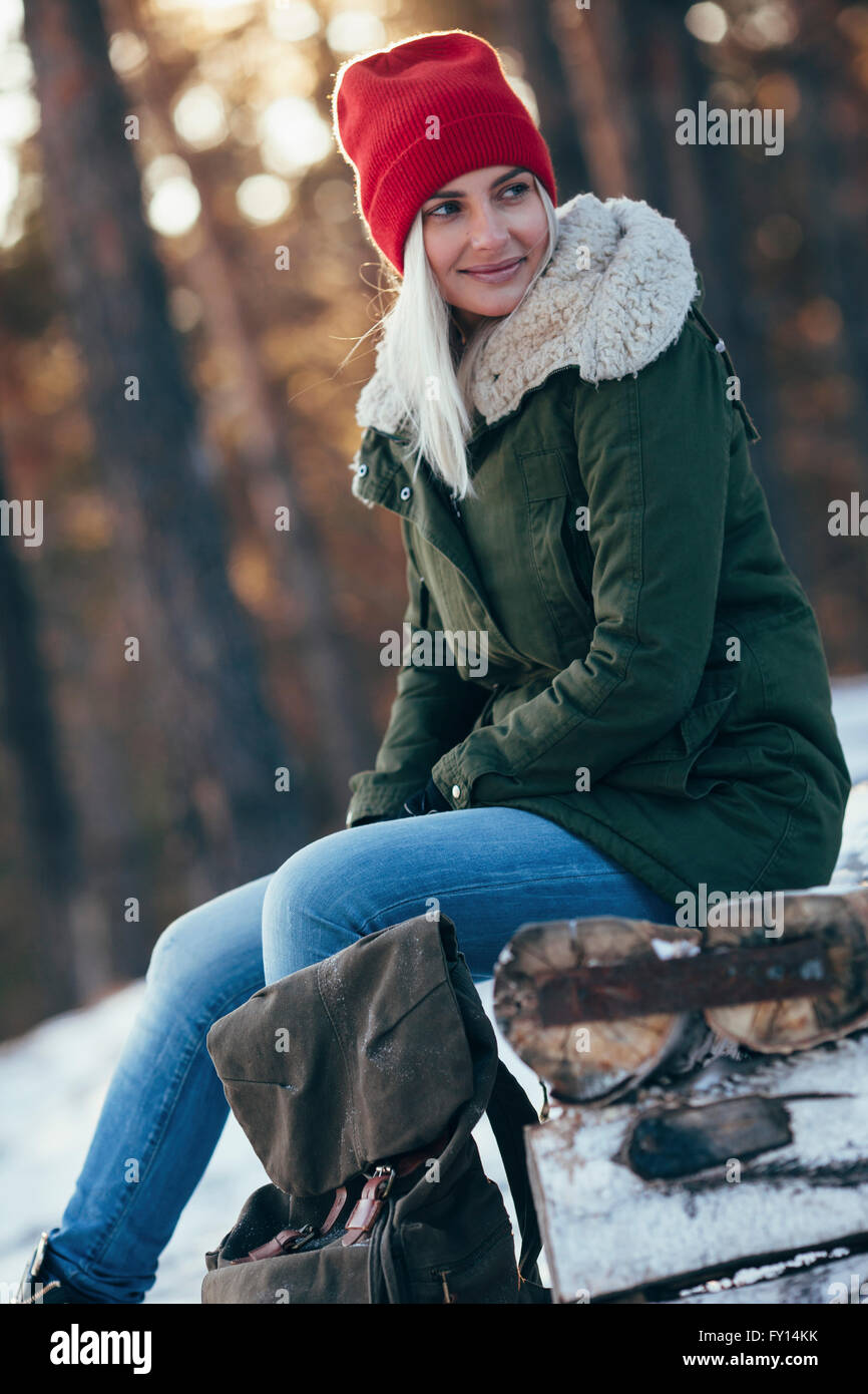 Young woman looking away while sitting on log pendant l'hiver Banque D'Images