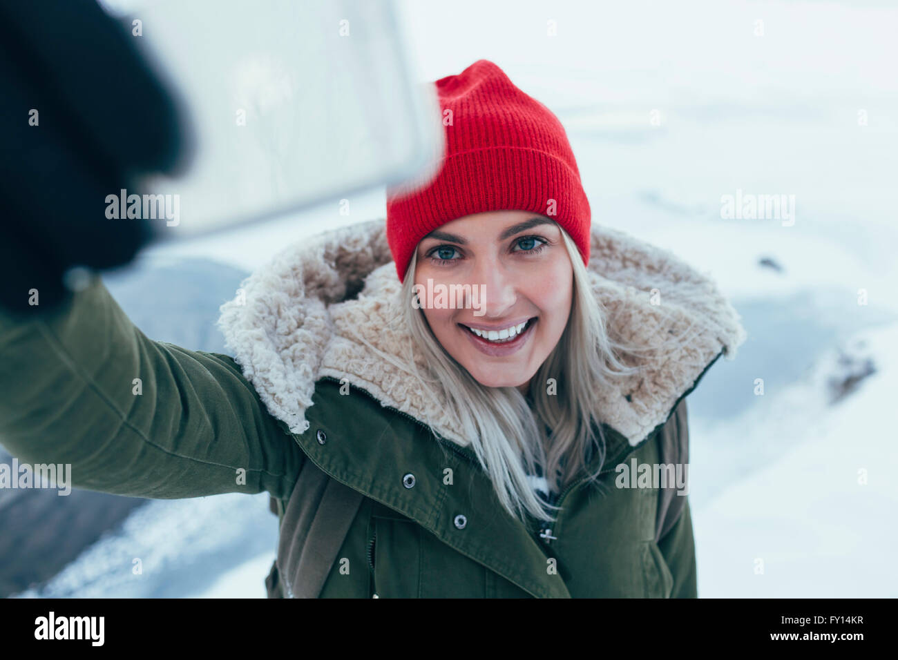 Smiling young woman on smart phone selfies en hiver Banque D'Images
