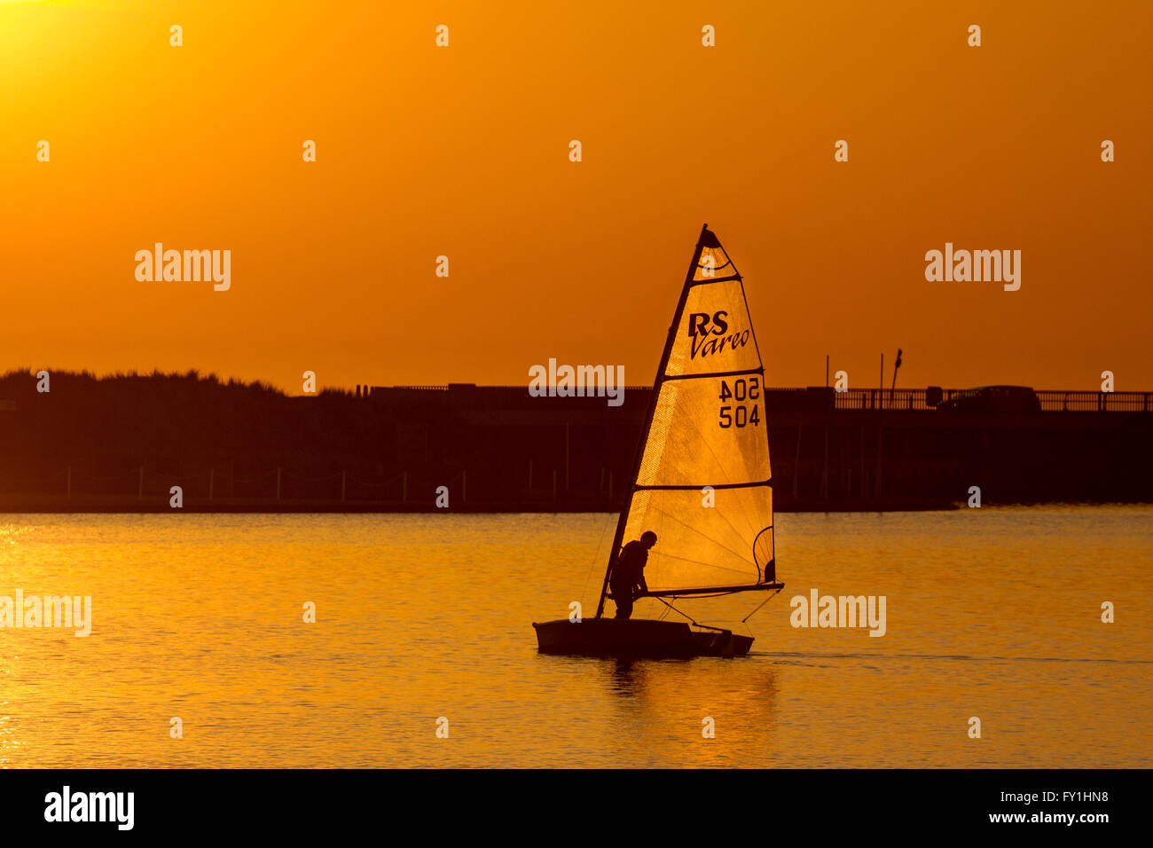 Bateau à voile terne au coucher du soleil sur le lac marin. Southport, Merseyside, le lac marin le 20 avril 2016. Météo britannique. Des vents légers et un Golden Coucher de soleil sur le lac marin comme James Ted 504 Club de voile de Southport RS Vareo voiles son yacht. Le bateau est un spinnaker powered-hander unique. La coque stable, réactive l'age, et de systèmes de manutention facile font de la RS Vareo défi réalisable dans de bonnes conditions- mais pas aujourd'hui. Banque D'Images