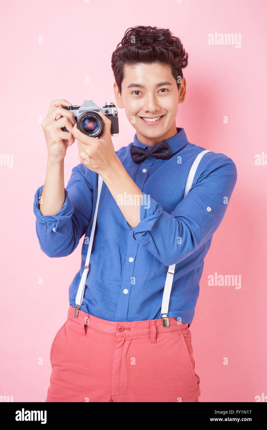 Smiling young man in retro style holding a camera fixant à l'avant Banque D'Images