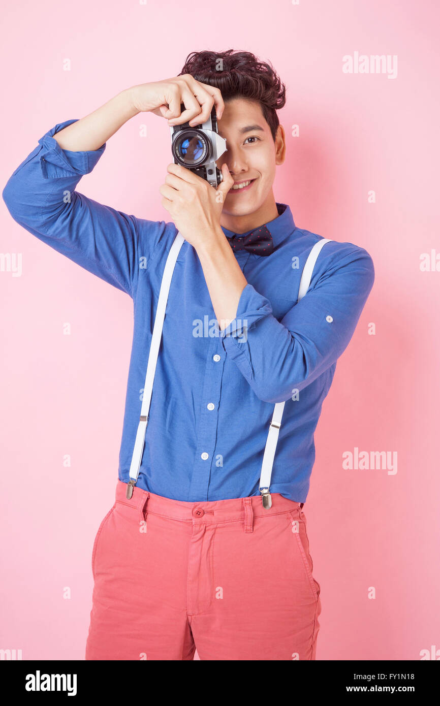 Smiling young man in retro style tenant un appareil photo et prendre une photo à regarder/ Banque D'Images