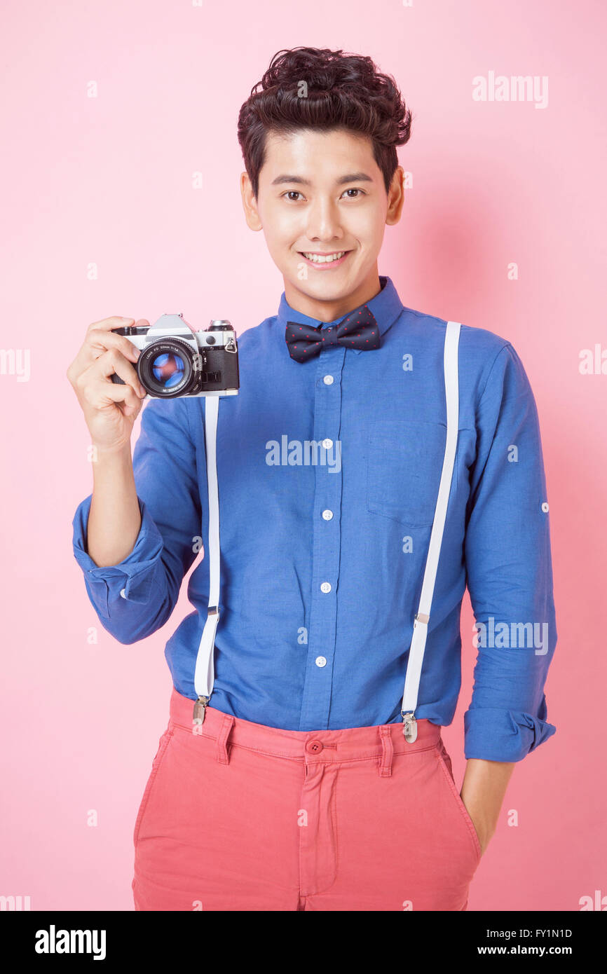 Smiling young man in retro style holding a camera plaçant une main dans la poche avant de Banque D'Images