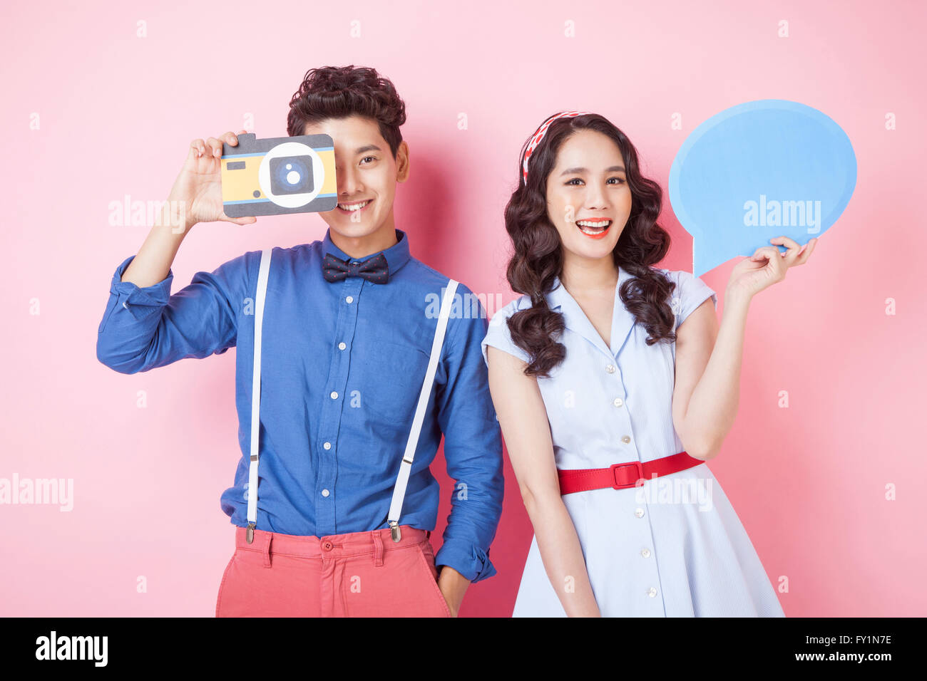 Portrait of young smiling couple in styles retro posant avec caméra et bulle à regarder/ Banque D'Images