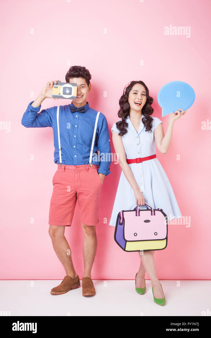 Young smiling couple in styles retro debout avec appareil photo, sac et bulle fixant à l'avant Banque D'Images