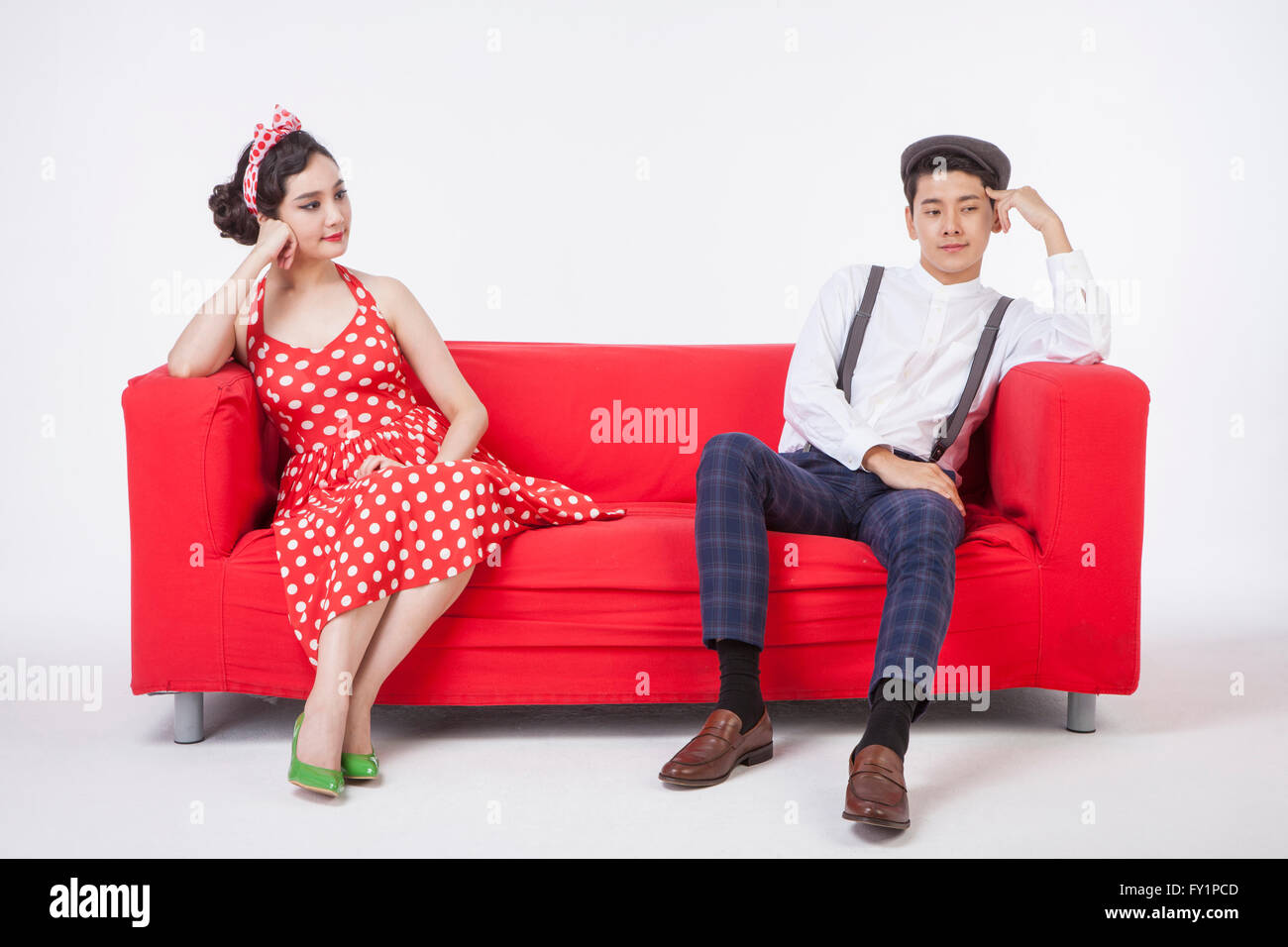 Jeune couple en styles retro assis sur un canapé avec le menton dans les mains Banque D'Images