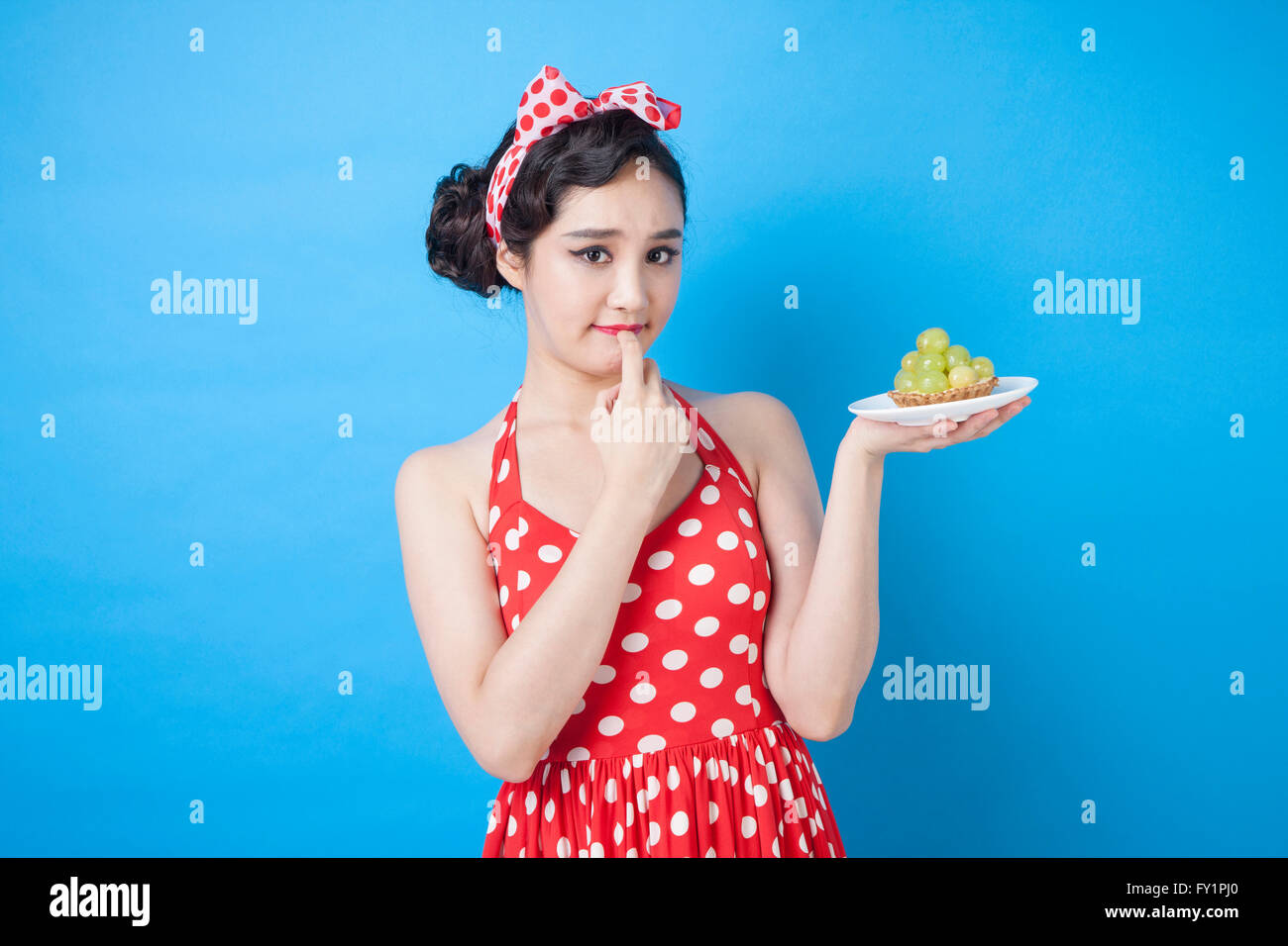 Portrait of young woman holding raisin vert sur une assiette et de toucher ses lèvres fixant à l'avant Banque D'Images