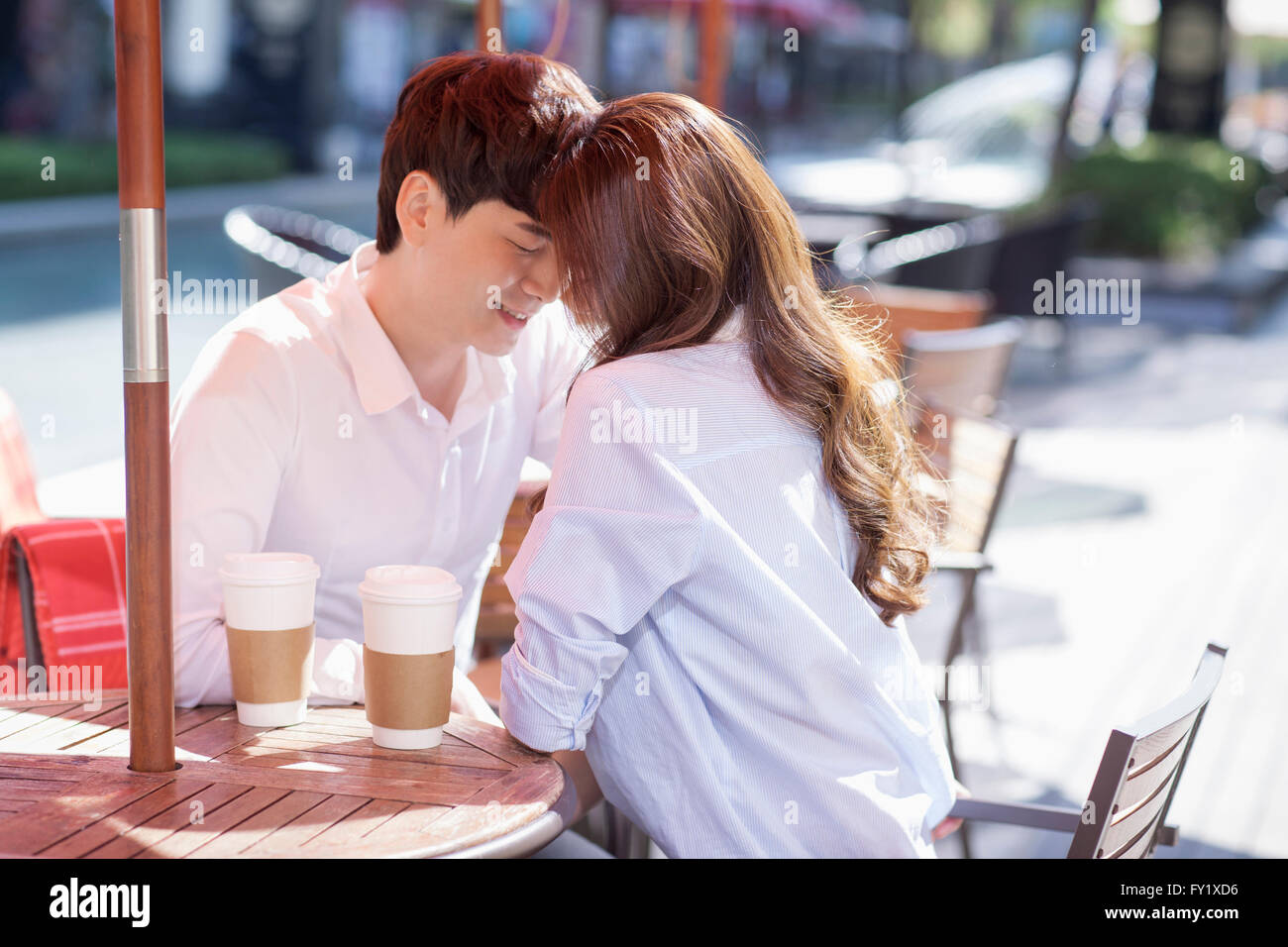 Couple de mettre leurs têtes ensemble à la terrasse d'un café avec du café sur la table Banque D'Images