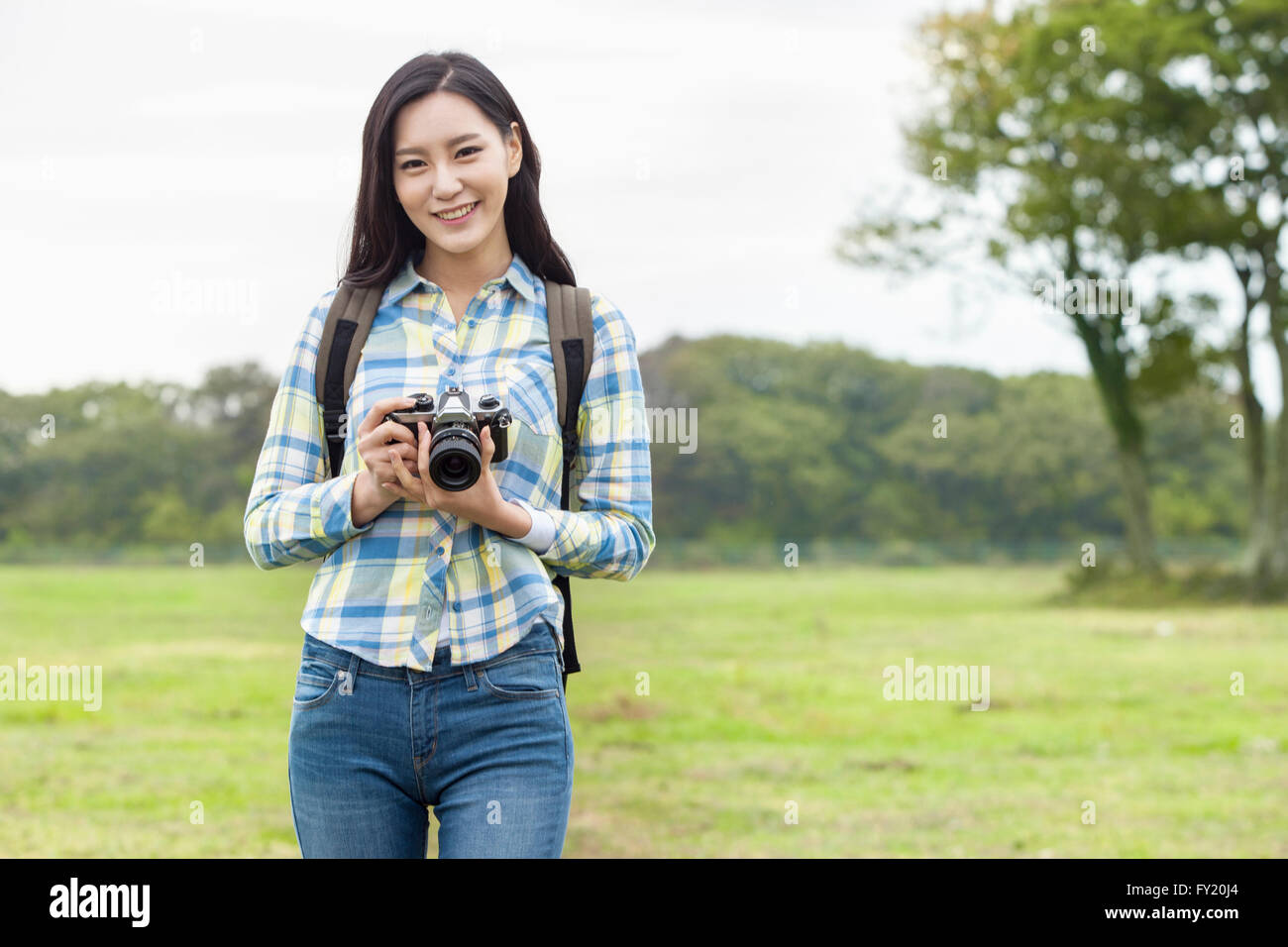 Sac à dos femme en holding a camera and smiling at green field Banque D'Images