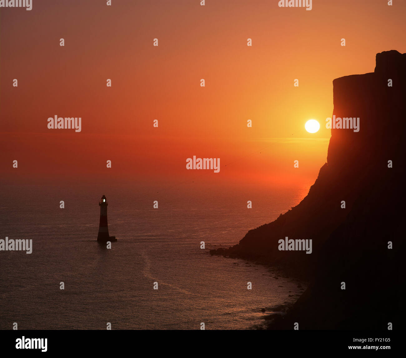 Le soleil derrière Beachy Head et le Beachy Head Lighthouse. Banque D'Images