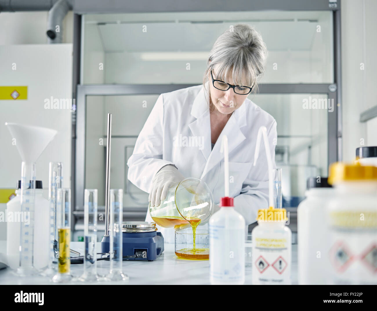 Chimiste analytique féminine, les cheveux gris, 50-55 ans, remplissage d'un mélange de produits chimiques de l'eau et le ferrocyanure de potassium dans un verre Banque D'Images